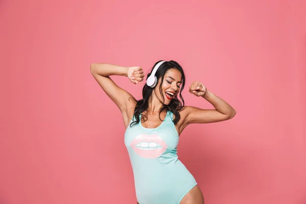 一个开朗的年轻女子的肖像在粉红色的泳装隔离 跳舞时 听音乐与耳机 — 图库照片