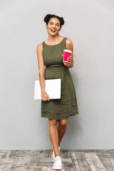 一个微笑的年轻女子在衣服隔离 携带笔记本电脑和外卖咖啡的肖像 — 图库照片