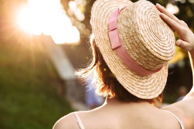 Arkadan görünüşü genç kadın elbise ve hasır şapka günbatımı açık havada poz