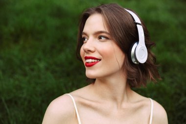 Gülümseyen kadın elbise ve süre uzağa arıyorsunuz ve parkta oturan müzik dinlerken kulaklık