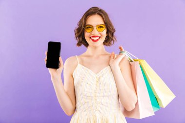 Genç kadın alışveriş torbaları cep telefonu görüntüsünü gösterilen tutan mor duvar arka plan üzerinde izole fotoğrafı.