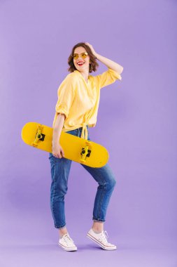 Kaykay, menekşe arka plan üzerinde izole ayakta tutan mutlu bir genç kız portresi tam uzunlukta