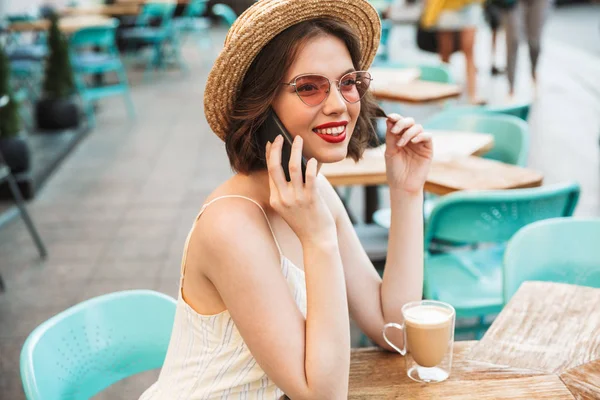 Side view of Smiling talking by smartphone while sitting by the table in city cafe