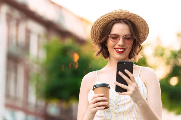 ドレス 麦藁帽子とスマート フォンを屋外で使うサングラスの笑顔の女性のイメージ — ストック写真