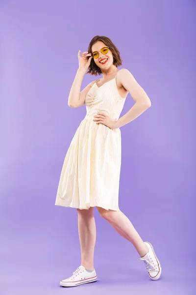 立っている 紫色の背景にカメラを見てポーズ夏服に身を包んだ笑顔の若い女性の完全な長さの肖像画 — ストック写真