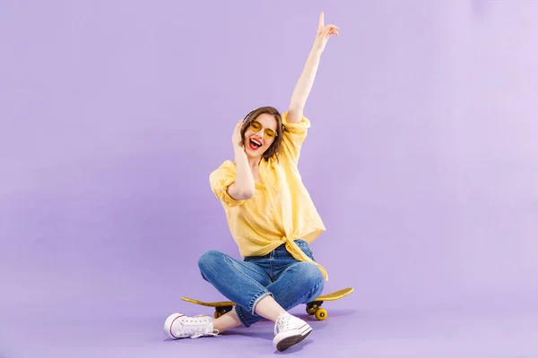 Porträtt Positiv Ung Flicka Hörlurar Sitter Skateboard Isolerade Över Violett — Stockfoto