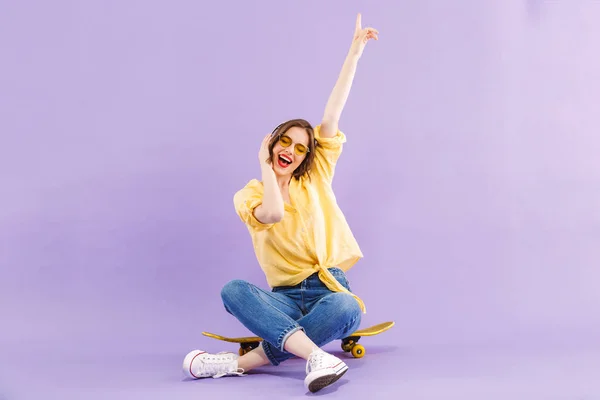 Retrato Uma Jovem Positiva Fones Ouvido Sentados Skate Isolado Sobre — Fotografia de Stock