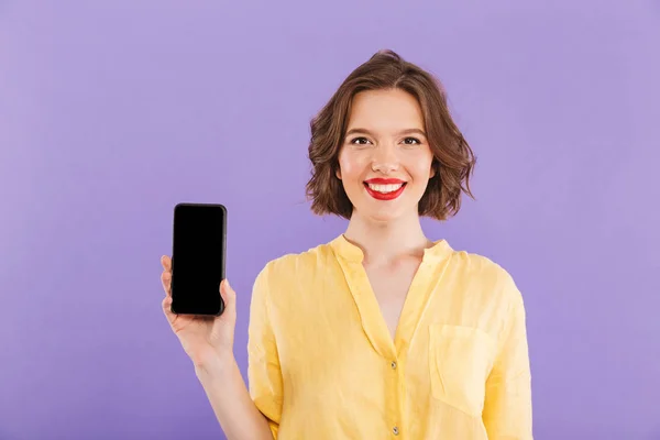 一个微笑的年轻女子的肖像显示空白屏幕手机在紫罗兰色背景下隔离 — 图库照片