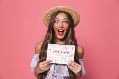 Photo of attractive glamour woman 20s wearing straw hat holding menses calendar isolated over pink background in studio clipart