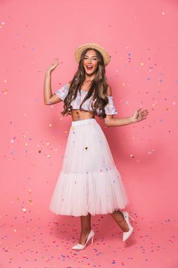 Yaz giysileri pembe bir arka plan üzerine konfeti yağmuru altında neşeli bir genç kızı tam uzunlukta portresi