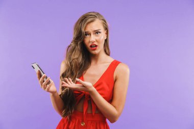 Görüntü closeup merak veya menekşe arka plan üzerinde izole cep telefonu ayakta tutarken sürpriz ifade çileden kadın 20'li yaşlarda giyen kırmızı elbise