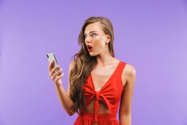 Görüntü closeup merak veya menekşe arka plan üzerinde izole cep telefonu ayakta tutarken sürpriz ifade sürpriz veya şok kadın 20'li yaşlarda giyen kırmızı elbise