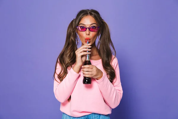 紫色の背景に分離されたストローで炭酸飲料を飲んでサングラスで素敵な女の子の肖像画 — ストック写真