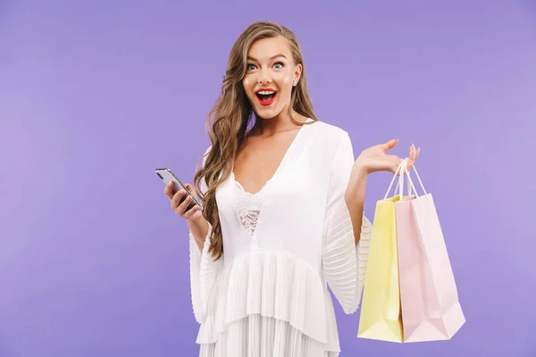 一个快乐的年轻女子的肖像 穿着白色礼服 站在独立的 鼓风机购物袋 使用手机 — 图库照片