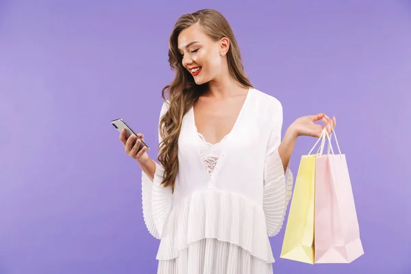 一个微笑的年轻女子的肖像 穿着白色的礼服 站立孤立 鼓风机购物袋 使用手机 — 图库照片