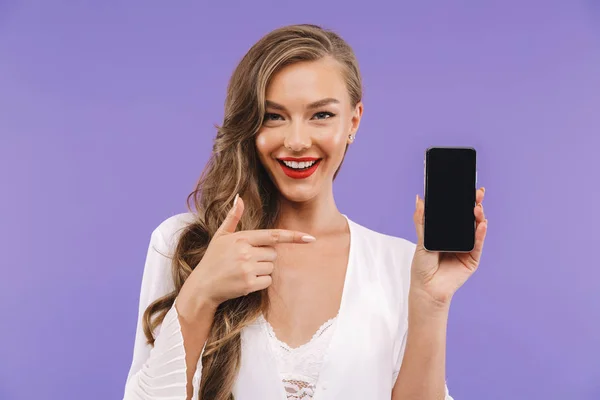 一个快乐的年轻女子的肖像站在白色的礼服站立孤立 指向空白屏幕移动电话 — 图库照片