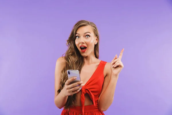 欢快兴奋的女人20S 穿着红色礼服微笑和手持手机站在紫色背景隔离的图像特写 — 图库照片