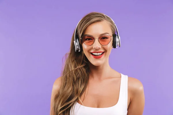 微笑的女人的肖像特写20S 在夏天衣服和太阳镜听音乐使用无线耳机在紫色背景下隔离 — 图库照片