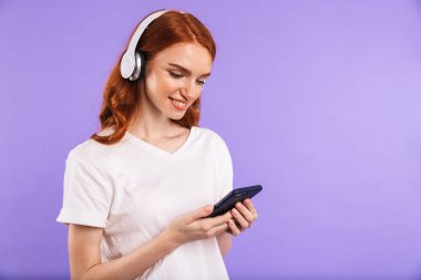 Cep telefonu, kulaklık ile müzik dinlemek tutan menekşe arka plan üzerinde izole bir gülümseyen genç kız ayakta portresi