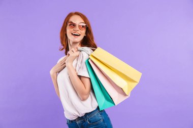 Neşeli bir genç kız uzağa arıyorsunuz alışveriş çantaları taşırken menekşe arka plan üzerinde izole duran güneş gözlüğü portresi