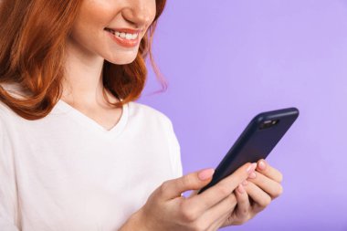 Cep telefonu kullaranarak menekşe arka plan üzerinde izole bir gülümseyen genç kız ayakta yakın çekim