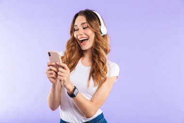 Kulaklık ile müzik dinlemek menekşe arka plan üzerinde cep telefonu tutan mutlu bir genç kız portresi izole