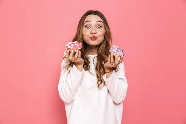一个可爱的年轻女子的肖像显示甜甜圈在粉红色背景下隔离 — 图库照片