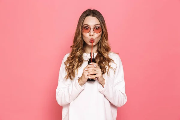 サングラス ピンク背景に分離されたストロー ボトルから炭酸飲料を飲む陽気な若い女性の肖像画 — ストック写真