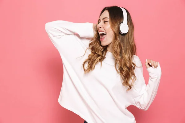 ピンクの背景に分離された音楽を聴くヘッドフォンで陽気な若い女性の肖像画 — ストック写真