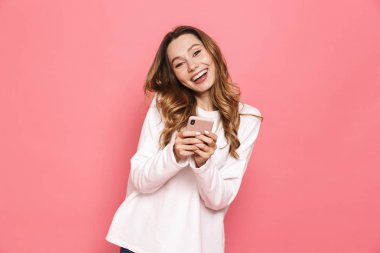 Cep telefonuyla pembe arka plan üzerinde izole mutlu bir genç kadın portresi