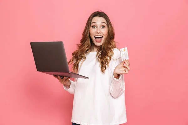 幸せな若い女性のラップトップ コンピューターを保持しているプラスチック クレジット カード ピンク背景に分離を示す肖像画 — ストック写真