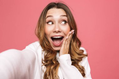 Selfie pembe arka plan üzerinde izole uzanmış el ile alarak neşeli bir genç kadın portresi