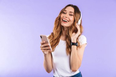 Kulaklık ile müzik dinlemek menekşe arka plan üzerinde cep telefonu tutan bir gülümseyen kız portresi izole