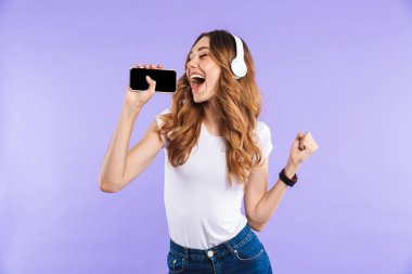 Şarkı kulaklık ile müzik dinlemek cep telefonu menekşe arka plan üzerinde izole holding neşeli genç bir kızın portresi