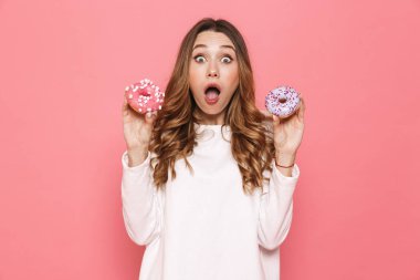 Pembe arka plan üzerinde izole donuts gösterilen sürpriz bir genç kadın portresi