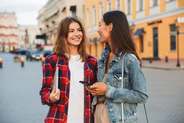 Zwei Lächelnde Junge Freundinnen Die Zusammen Der Stadtstraße Stehen Laptop — Stockfoto