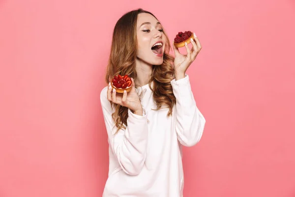 一个满意的年轻女子的肖像 在粉红色的背景下吃糕点隔离 — 图库照片