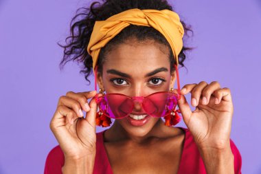 Güneş gözlüğü ile poz menekşe arka plan üzerinde kafa bandı içinde gülümseyen genç Afrikalı kadın portresi kadar kapatın