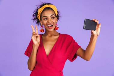 Menekşe arka plan üzerinde duran, bir selfie alarak kafa bandı içinde gülümseyen genç Afrikalı kadın portresi