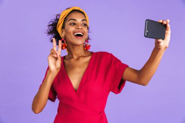 Menekşe arka plan üzerinde duran, bir selfie alarak, barış gösterilen kafa bandı içinde gülümseyen genç Afrikalı kadın portresi