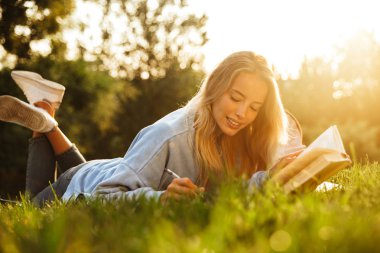 Notlar alarak bir kitap okuma çok hoş bir genç kız parkta, çimlerin üzerine döşeme sırt çantası ile portresi