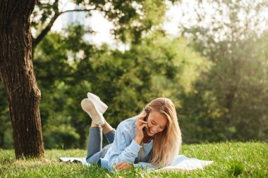 Cep telefonu üzerinde konuşurken parkta bir çim üzerinde döşeme bir sevimli genç kız portresi