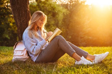 Notlar alarak bir kitap okuma bir ot parkta oturan bir neşeli genç kız portresi
