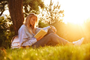 Notlar alarak bir kitap okuma bir ot parkta oturan olumlu genç bir kızın portresi