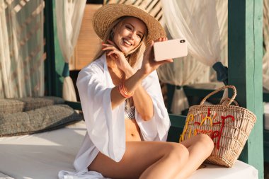 Bir selfie outsretched el ile alarak memnun genç kız yaz şapka ve plajda, vakit mayo