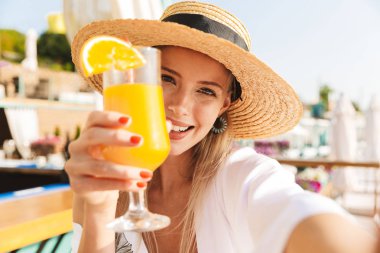 Genç ve güzel kız yaz şapka ve güneşli kumsalda dinlenme, bir kokteyl ile bir kafede oturan, bir selfie alarak mayo