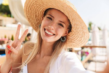 Barış gösterilen bir selfie alarak mutlu genç kız yaz şapka ve güneşli kumsalda, dinlenme mayo