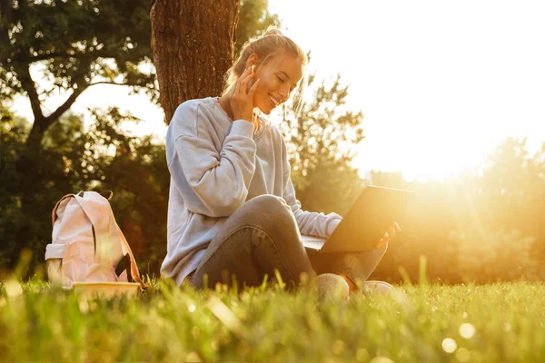 Portrait Cheerful Young Girl Earphones Backpack Sitting Legs Crossed Grass — Stock Photo, Image