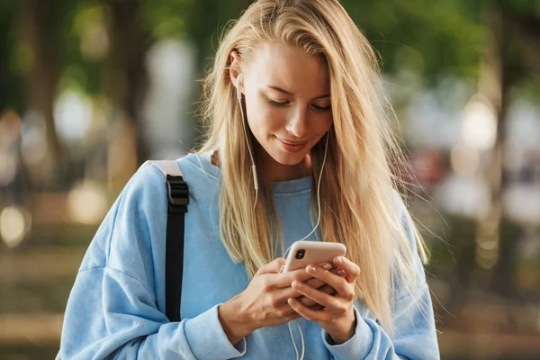 Cep telefonu tutan earphones Park'ta yürüyüş sırt çantası ile bir güzel genç kız öğrenci portresi