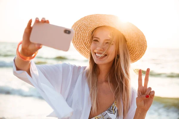 Outsretched の手で Selfie を取って夏帽子と水着 ビーチで時間を過ごす美しい若い女の子 — ストック写真